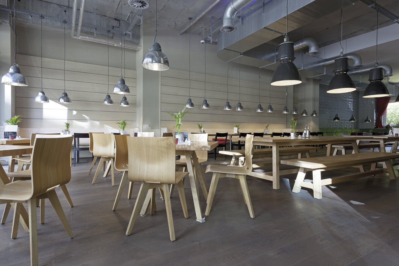 Geräumiger, heller Innenraum mit Holztischen und einem modernen Fliesenboden in Betonoptik.