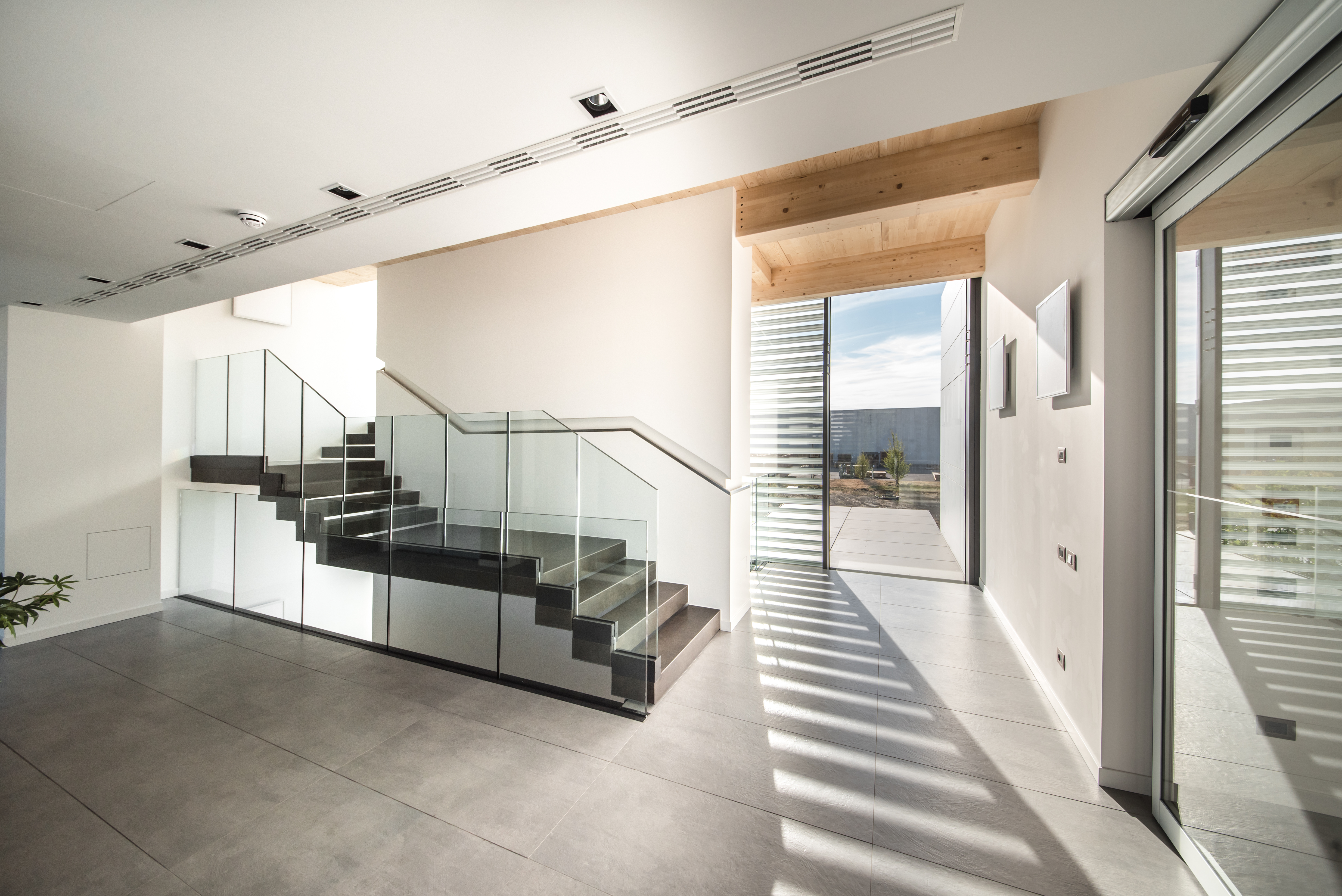 Hochwertige Bodenfliesen in Betonoptik im modernen Foyer mit eleganter Glastreppe.