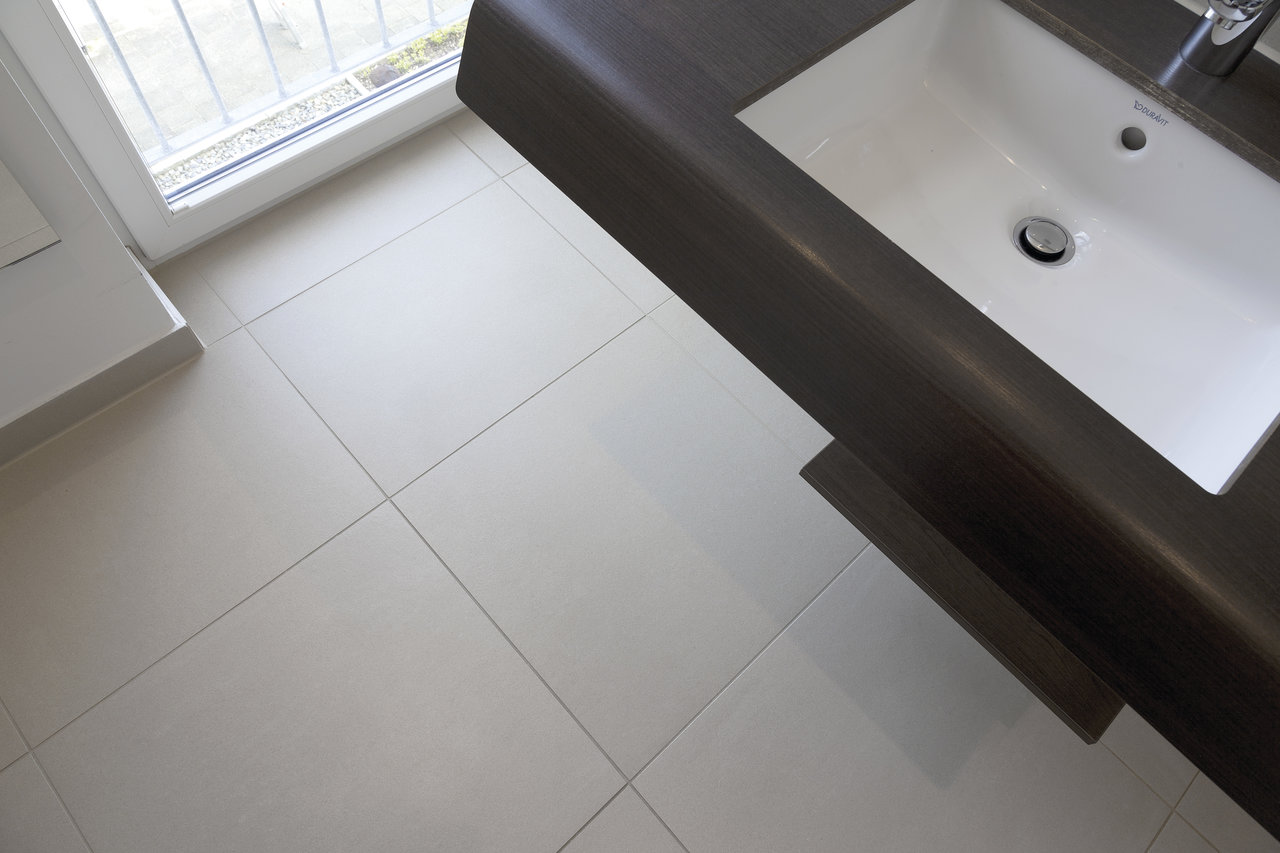 Helle, moderne Bodenfliesen im Badezimmer neben einem dunklen Waschtisch.