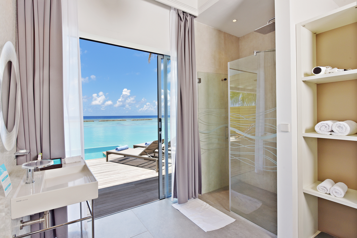 Helle Fliesen im modernen Badezimmer mit offener Dusche und direktem Zugang zur Terrasse mit Meerblick.