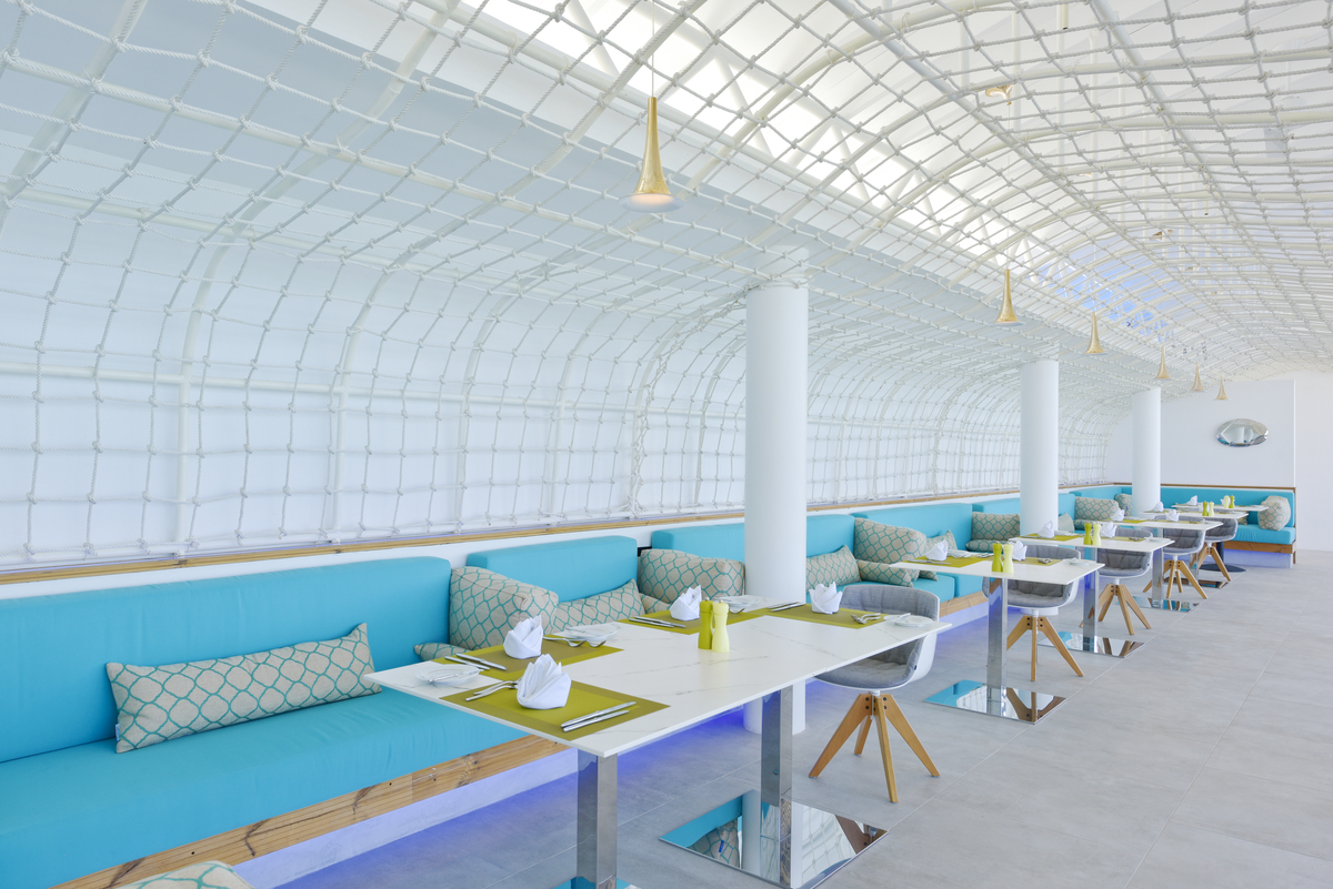 Modernes Restaurantinterieur mit hellen Fliesen und türkisen Polsterbänken.