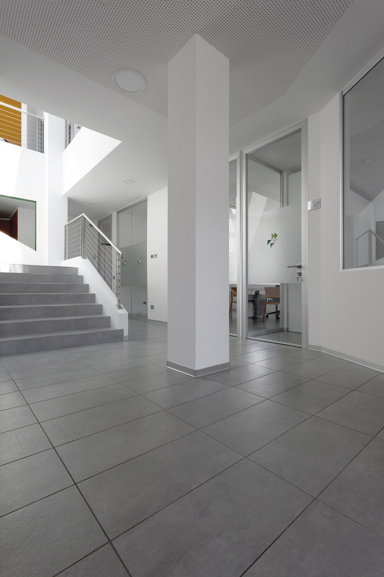 Großformatige graue Bodenfliesen in einem hellen, modernen Foyer mit Treppe.
